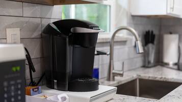 En kaffemaskine på en bordplade med en vask og et vindue i baggrunden.