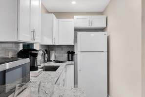 A modern kitchen with white cabinets, a built-in microwave, a coffee maker, and a stainless steel sink. - Stylish/Open Studio w/ Kitchen & Outdoor Space (Lake Worth)