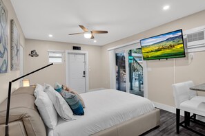 A bedroom with a bed, a desk, a chair, a ceiling fan, a TV, and a door. - Stylish/Open Studio w/ Kitchen & Outdoor Space (Lake Worth)