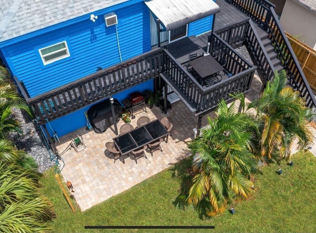 Une maison bleue dotée d’un patio comprenant une table et des chaises, le tout entouré de palmiers.