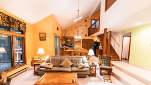 A spacious living room with a sofa, coffee table, and a dining area in the background. - GreatRoom, soaring ceilings, window walls,F/Place Just what you are looking for. (Bushkill)