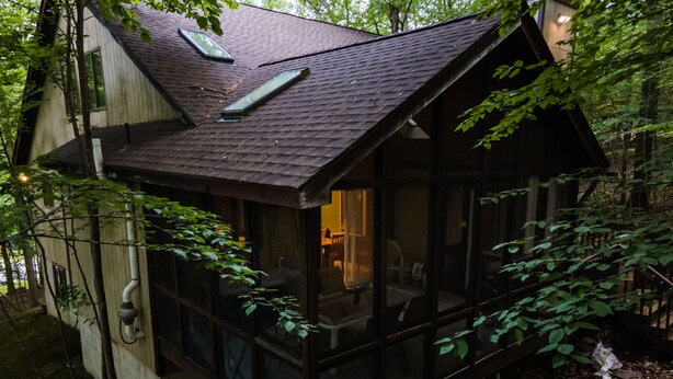 A small, dark wooden cabin with large windows, surrounded by dense foliage. - GreatRoom, soaring ceilings, window walls,F/Place Just what you are looking for. (Bushkill)