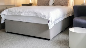 A modern bedroom with a large bed, a grey upholstered bench, and a white side table.