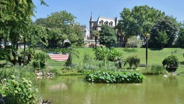 Un edificio storico con una torre, immerso nel verde e con uno stagno.