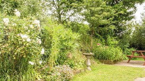 A garden with a stone birdbath, a wooden picnic table, and various flowering plants. - 2 bedroom accommodation in Hartland (Hartland)