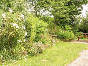Un giardino con una fontana per uccelli in pietra, un tavolo da picnic in legno e diverse piante fiorite.