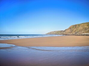 A beach with a clear sky, calm sea, and a rocky cliff. - 2 bedroom accommodation in Hartland (Hartland)