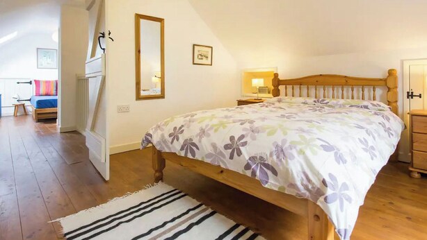 A bedroom with a wooden bed, a nightstand, a mirror, and a door. - 2 bedroom accommodation in Hartland (Hartland)