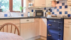 A kitchen with wooden cabinets, a microwave, a stove, and a window with greenery outside. - 2 bedroom accommodation in Hartland (Hartland)
