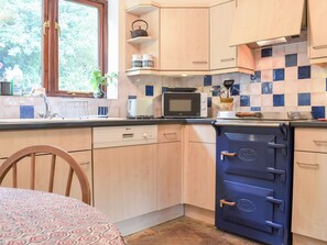 Cucina con mobili in legno, un forno a microonde, un fornello e una finestra affacciata sul verde.