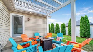 Een terras buiten met blauwe en oranje Adirondack-stoelen, een vuurkuil en een pergola.