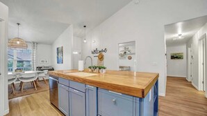 Een moderne keuken met een houten aanrechtblad, blauwe keukenkastjes en een 'welcome'-bord aan de muur.