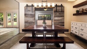 A dining area with a dark wooden table, white upholstered chairs, a potted plant, and a modern fireplace with a stone wall backdrop. - Bright Centrally located home in Sedona (Sedona)