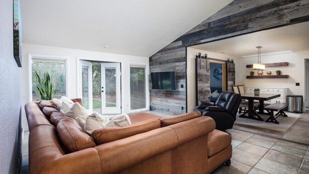 A modern living room with a leather sofa, a dining area with a table and chairs, and a large window with a view of the outdoors. - Bright Centrally located home in Sedona (Sedona)