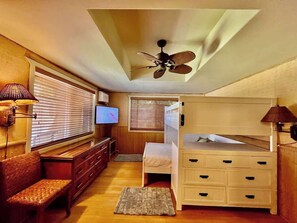 A compact bedroom with a bunk bed, a television, a desk, and a ceiling fan. - Bamboo Beach Cottage ~ Steps from shoreline access (Waimea)