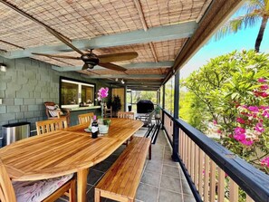 A covered outdoor dining area with a wooden table, benches, and a grill.