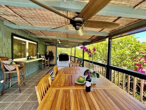 A covered outdoor dining area with a wooden table, chairs, and a ceiling fan.