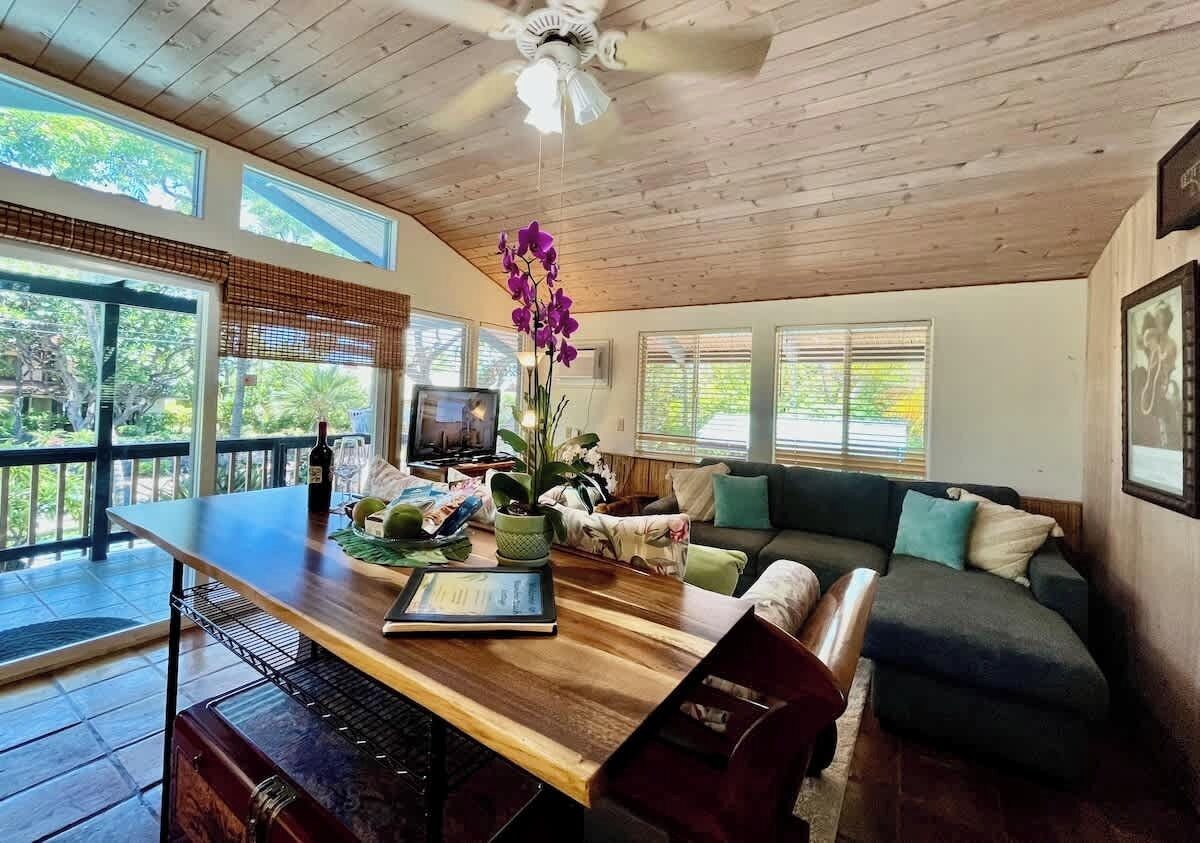 A spacious living area with a wooden ceiling, a large window, a sofa, a coffee table, and a television.