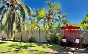 A backyard with a wooden fence, a palm tree, and a red umbrella.