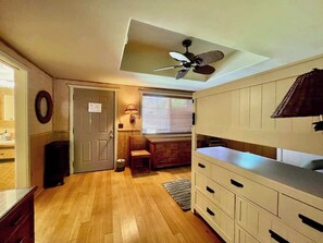 A compact kitchen with wooden flooring, a ceiling fan, a window with blinds, and a door leading to another room. - Bamboo Beach Cottage ~ Steps from shoreline access (Waimea)