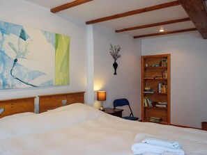 Een slaapkamer met een groot bed, een houten hoofdbord, een boekenkast, een wandvaas en een schilderij.