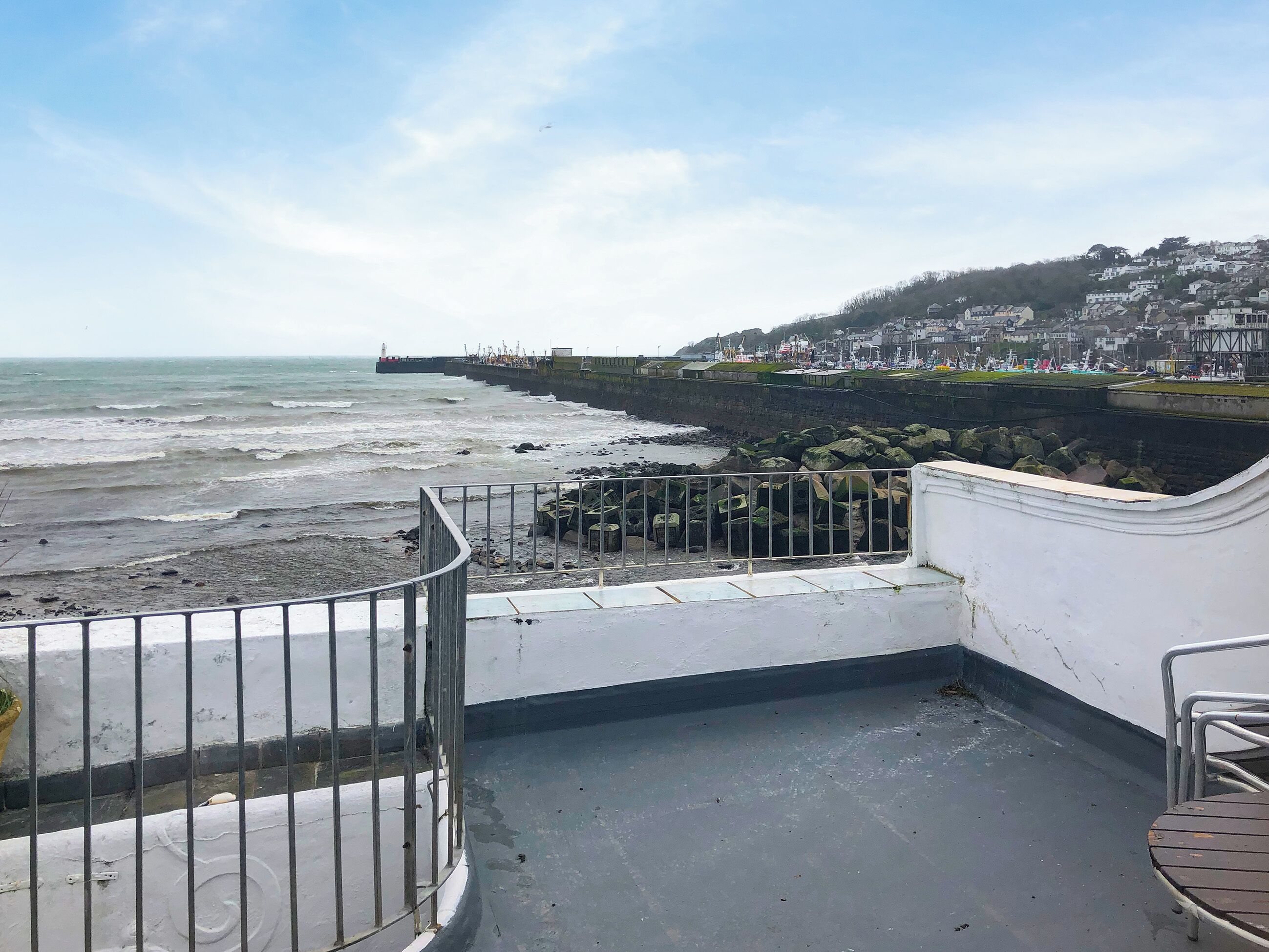 A coastal view with a rocky shoreline, a pier, and a town in the background.