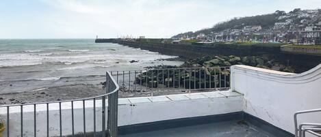 Vista costera con un litoral rocoso, un muelle y un pueblo al fondo.