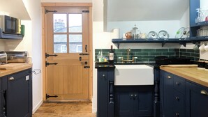 A kitchen with dark cabinets, a wooden door, a sink, and a microwave. - Reverse level cottage in Newlyn stunning sea views from the roof top balcony. (Newlyn)