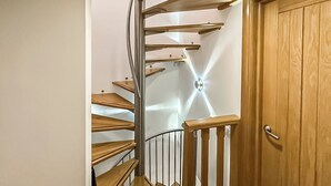 Un escalier en colimaçon avec des marches en bois et des rampes en métal, menant à une porte dotée d’un cadre en bois.