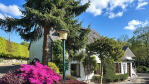 Una casa con encanto con un muro de piedra, un poste de luz y un pequeño jardín con flores rosas.