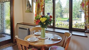 Comedor con una mesa dispuesta para cuatro, un jarrón de flores y una ventana con cortinas.