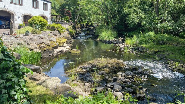 Una casa de piedra con jardín y arroyo.