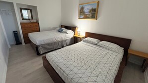 A bedroom with two beds, a dresser, a nightstand, a lamp, and a painting on the wall. - Waterfront Cottage on the Upper Rideau Lake (Westport)
