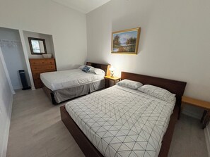 A bedroom with two beds, a dresser, a nightstand, a lamp, and a painting on the wall.