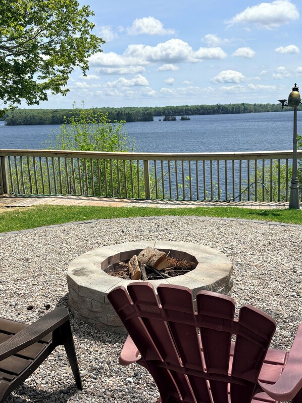 A deck with a fire pit, Adirondack chairs, and a view of a lake.