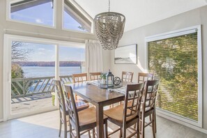 Enjoy meals in this dining area with a large table and six chairs, surrounded by a high ceiling and large windows offering a view of the water.
