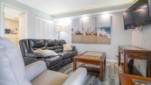 Een woonkamer met een leren bank, een salontafel en een flatscreen televisie aan de muur.
