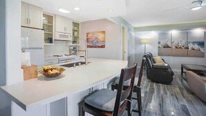 Een moderne keuken met witte kasten, een centraal eiland en een zithoek met een bank en stoelen.