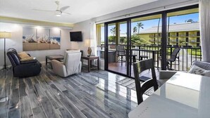 Een ruime woonkamer met een modern design, inclusief een flatscreen televisie, comfortabele zithoek en een balkon met buitenmeubilair.