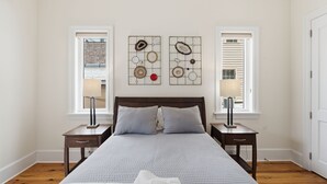 Quarto com cama, duas mesas de cabeceira, uma janela e uma obra de arte na parede.