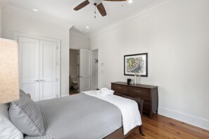 Une chambre à coucher avec un lit, une commode, un ventilateur de plafond et un tableau encadré au mur.