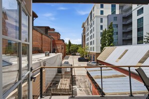 Une vue depuis un balcon donnant sur une rue bordée d’immeubles modernes, un parking et un ciel dégagé.