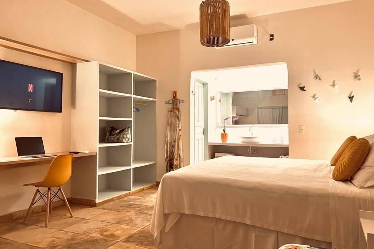 A bedroom with a bed, a desk with a laptop, a TV, and a wardrobe.