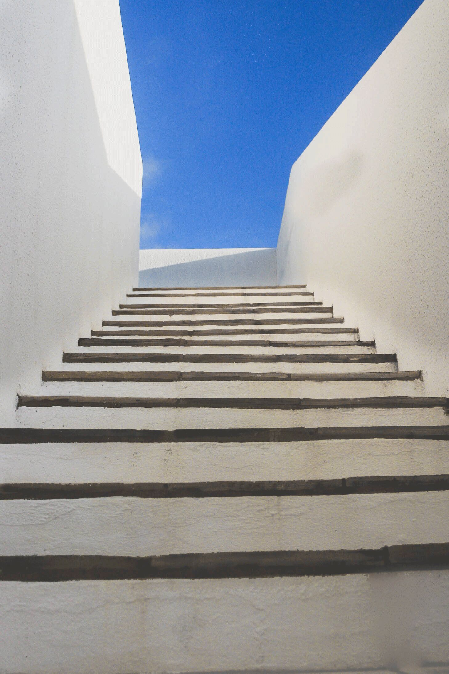 Uma escadaria que sobe, com paredes brancas e um céu azul claro acima.