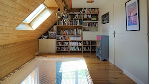 Ein Zimmer mit schrägem Dach, Holzregalen, einer kleinen Kommode und einem gerahmten Bild an der Wand.