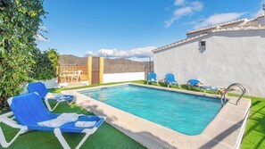 A swimming pool with blue lounge chairs, a white wall, and a clear sky.
