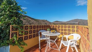 Ein Balkon mit Tisch, Stühlen, einer Pflanze und Blick auf Hügel.
