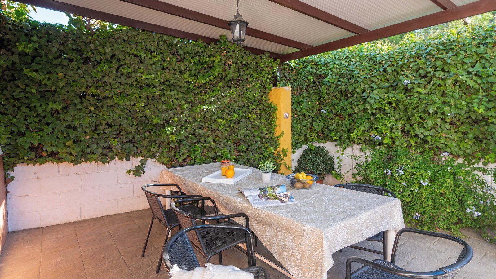 An outdoor patio with a table set for two, surrounded by chairs, and a yellow pillar.