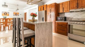 A modern kitchen with wooden cabinets, a marble countertop, a built-in oven, and a dining area with chairs and a table.