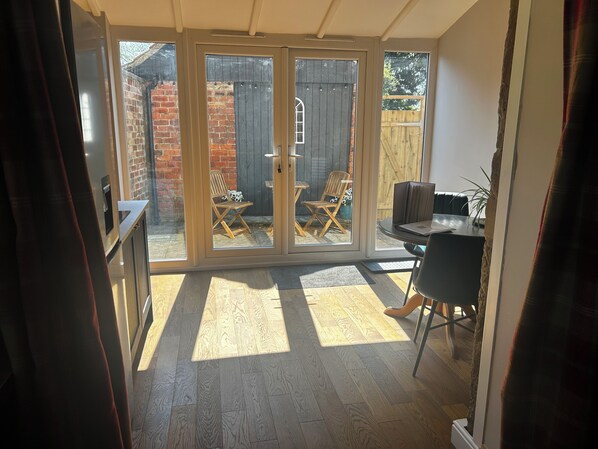 A room with a sliding glass door leading to a patio, a small table with chairs, and a wooden floor.